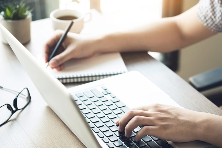 young man is taking a note on a notebook from the internet research using laptop computer. learning with technologies concept.